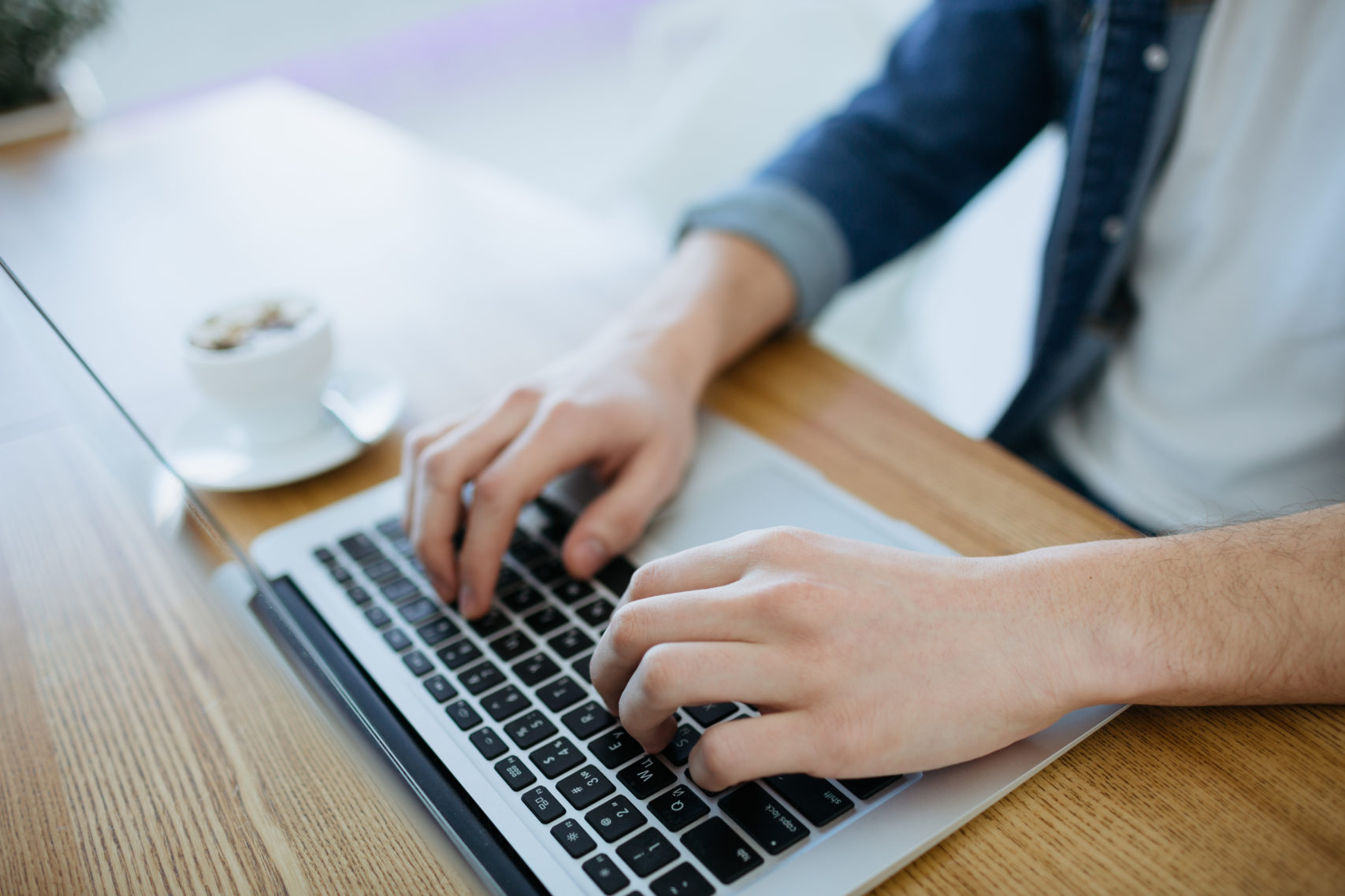 man typing on a macbook with a cup of coffee nearby